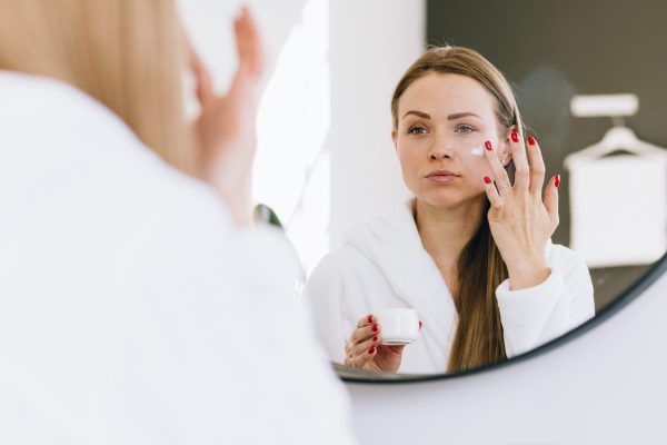 Woman applying face cream in a mirror, illustrating ways to revitalize tired-looking skin