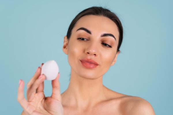 Woman holding a makeup sponge, illustrating how to apply makeup on dry skin without flaking
