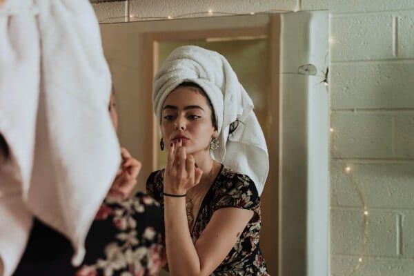 Woman applying makeup in a mirror, illustrating makeup tips to brighten dull and tired-looking skin