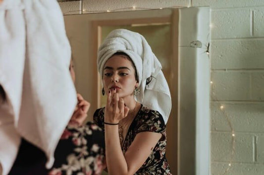 Woman applying makeup in a mirror, illustrating makeup tips to brighten dull and tired-looking skin