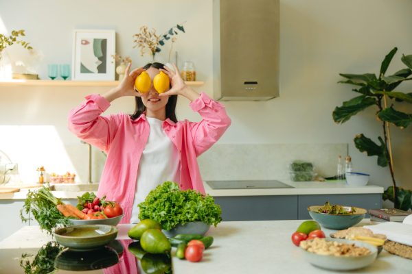 Woman holding lemons in a kitchen with fresh fruit and vegetables for healthy glowing skin