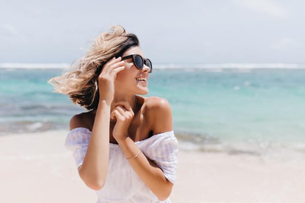 Woman at the beach wearing sunglasses, representing summer makeup tips for a long-lasting look