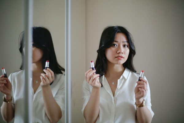 Woman choosing lipstick in a mirror, illustrating makeup mistakes that can make skin look dull and older