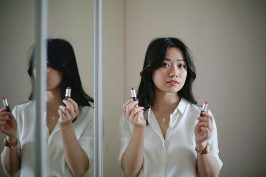 Woman choosing lipstick in a mirror, illustrating makeup mistakes that can make skin look dull and older