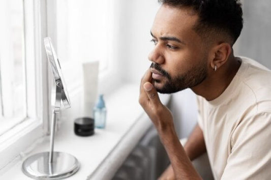 Man examining his skin in a mirror, illustrating essential skincare tips and products for men